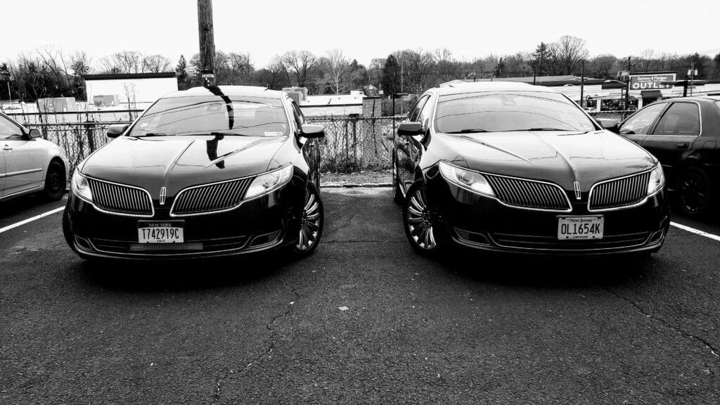 Two black Lincoln MKS sedans parked side-by-side with NY and NJ limo plates